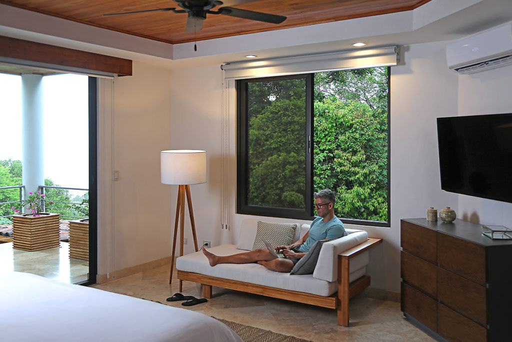 Man sitting on the couch at his room at Casa Anjali, while he is working on his laptop.